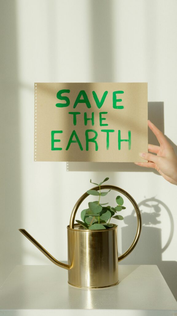 pexels photo 7048259 7048259 A hand holds a sign reading 'SAVE THE EARTH' above a brass watering can with a eucalyptus plant on a white background.